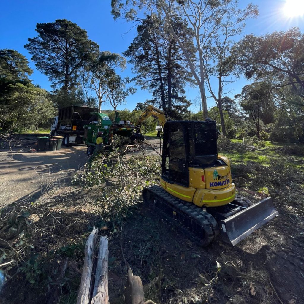 A compact yellow machine is positioned on the ground next to a tree, surrounded by grass and dirt.
